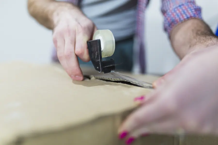 Handen plakken een verhuisdoos dicht met tape